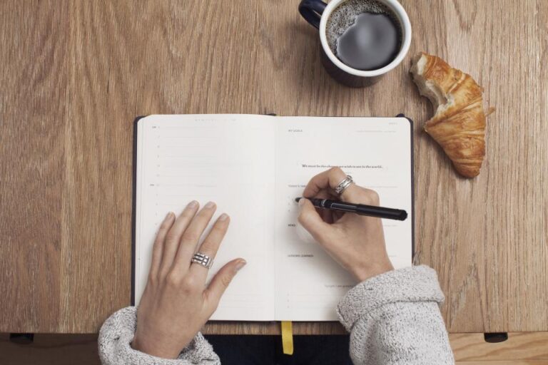 Person writing gratitude journal at breakfast table with coffee, illustrating a morning gratitude practice